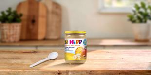 HiPP Frucht & Getreide Feines Bircher-Müesli Bio-Babygläschen auf Holztisch mit Löffel in heller Küche