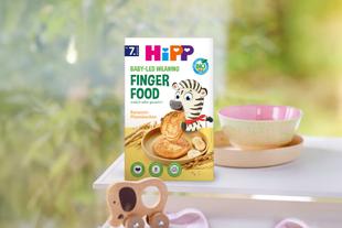 Packung HiPP Finger Food mit gezeichnetem Zebra und Getreideähren auf dem Tisch neben einer Schale