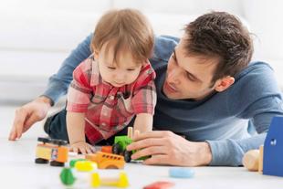 Ein kleines Kind und ein Erwachsener, bei dem es sich vermutlich um ein Elternteil handelt, spielen mit buntem Spielzeug auf dem Boden.