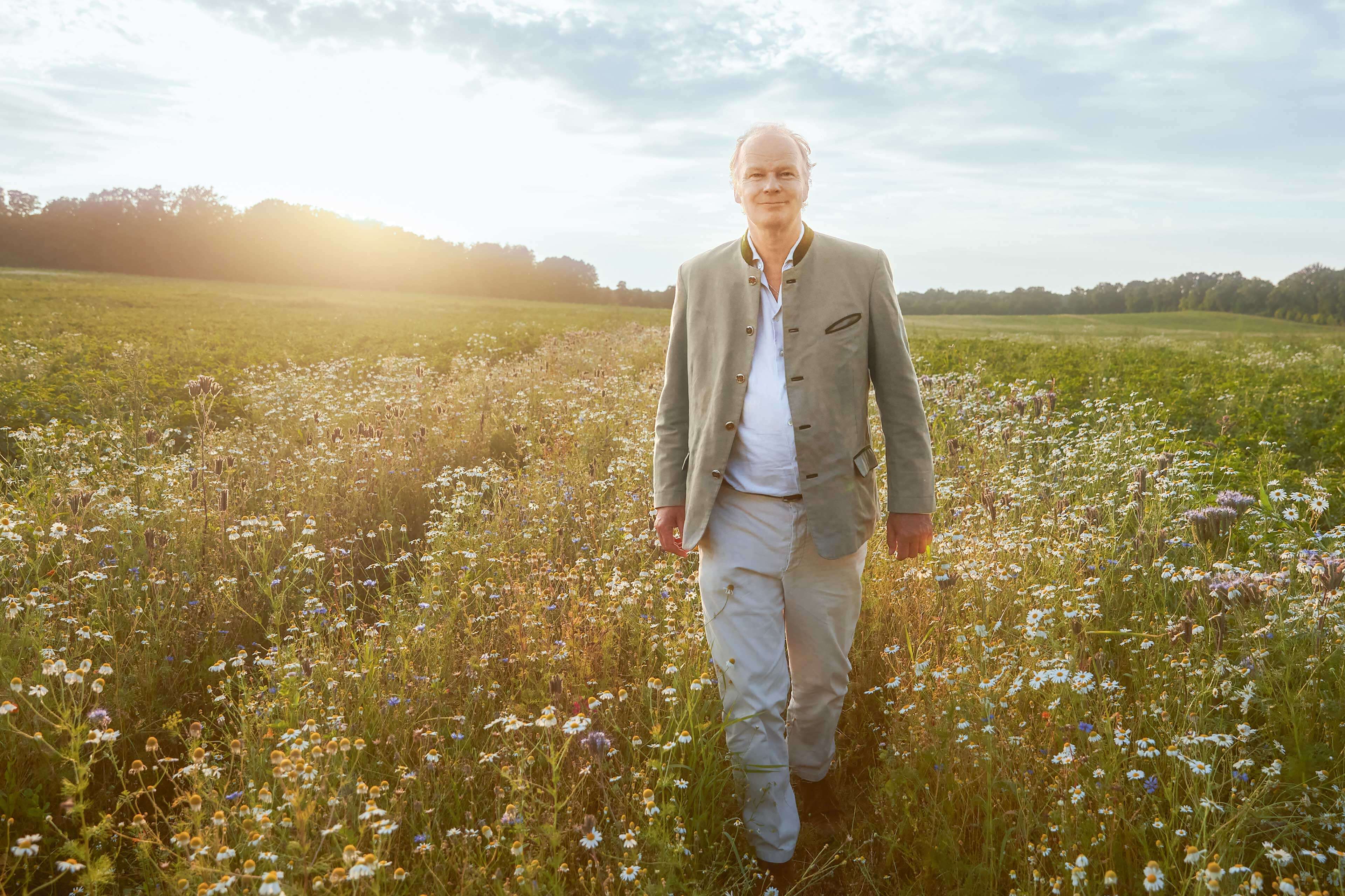 Stefan Hipp geht bei Sonnenuntergang durch eine blühende, naturbelassene Wiese und blickt zufrieden in die Ferne.