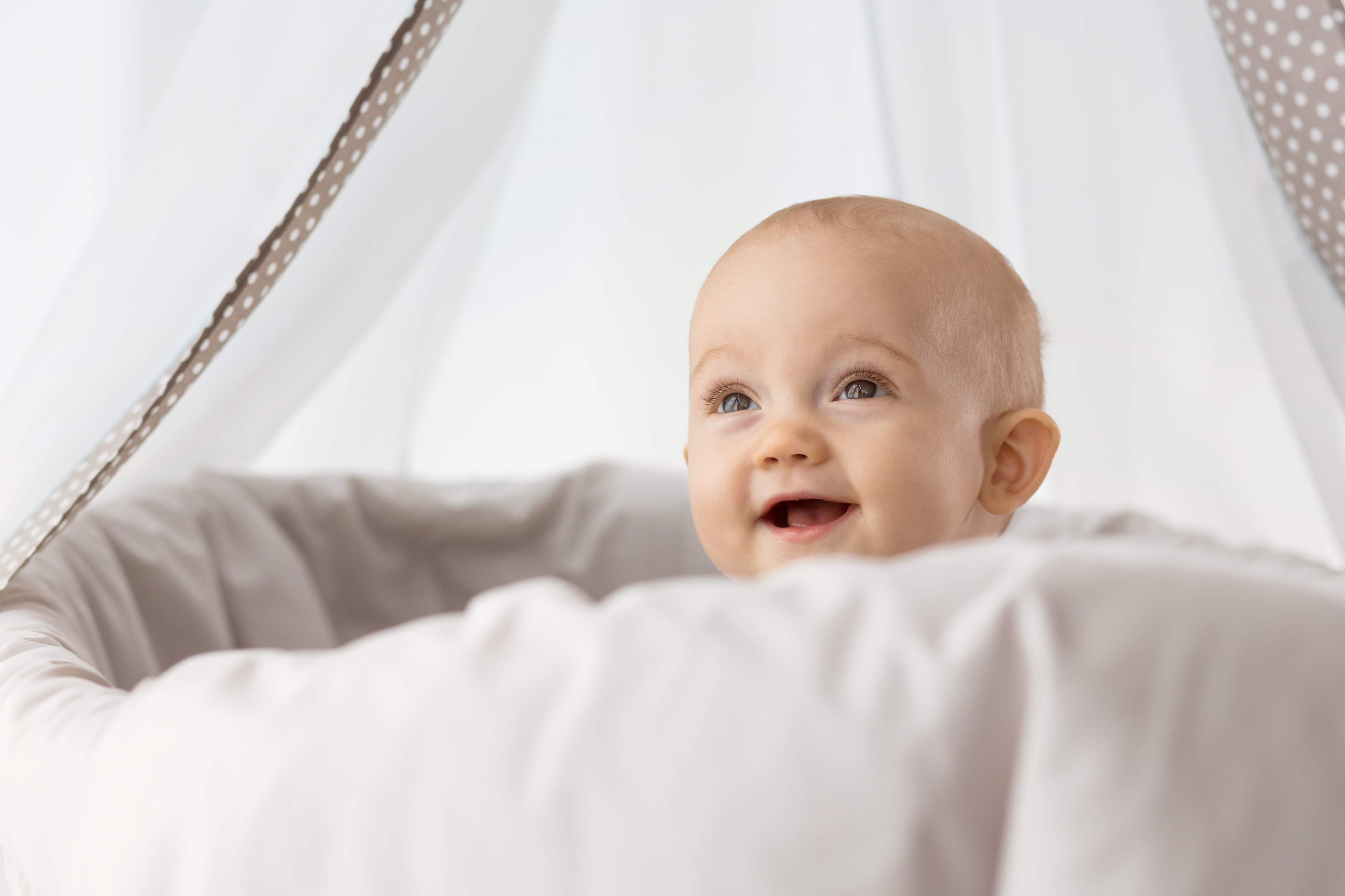 Ein Baby mit blauen Augen, das hinter einem weißen Tuch hervorlugt, mit einem neugierigen Gesichtsausdruck.
