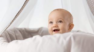 Ein Baby mit blauen Augen, das hinter einem weißen Tuch hervorlugt, mit einem neugierigen Gesichtsausdruck.
