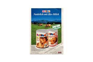 Historische HiPP-Anzeige für Bio-Säuglingsmilch mit zwei Milchdosen im Vordergrund und grasenden Kühen auf grüner Almwiese.