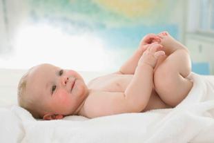 Ein Baby, das auf einem weißen Handtuch liegt, seine Füße hochhält und auf seine Hände schaut.