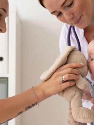 Nurse checking over baby whilst mum distracts him with a teddy bear
