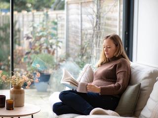 Pregnant mum sat on sofa reading book and drinking tea