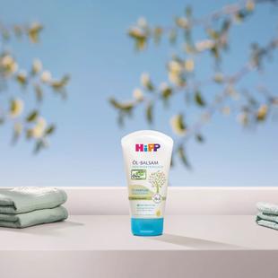 HiPP HOCHVERTRÄGLICH Öl-Balsam Tube vor blauem Himmel, flankiert von weichen Babyhandtüchern, für trockene, empfindliche Babyhaut