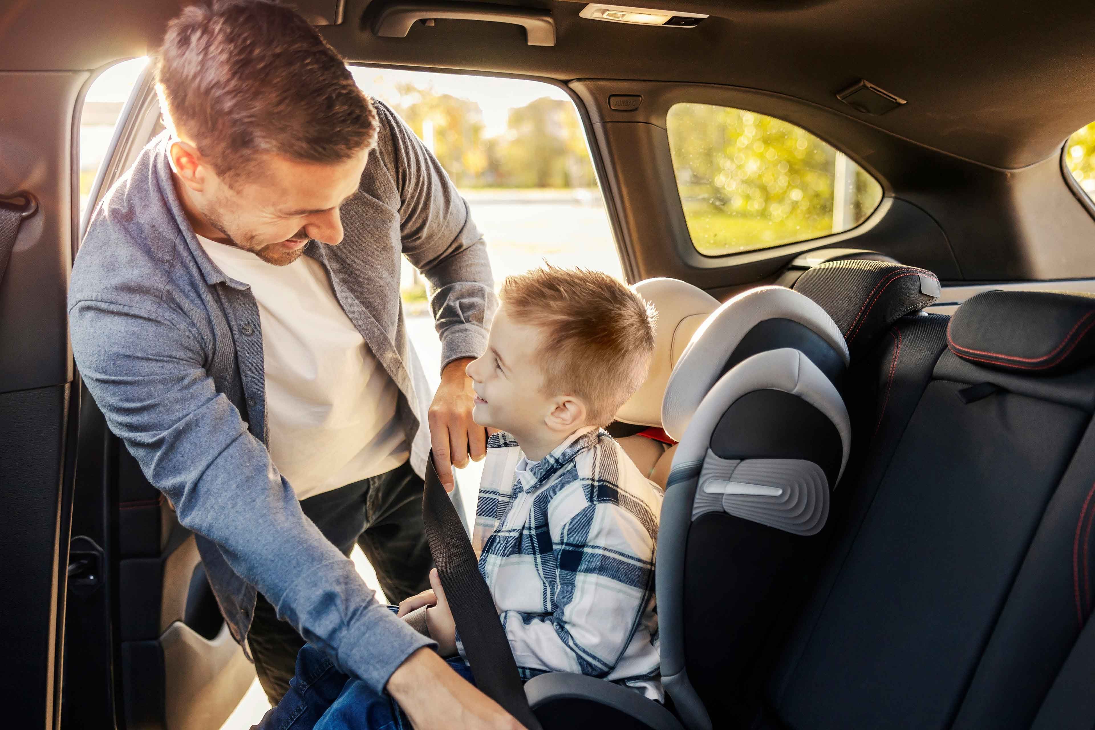Ein Mann kümmert sich um einen kleinen Jungen in einem Auto und stellt sicher, dass er sicher in einem Kindersitz sitzt.