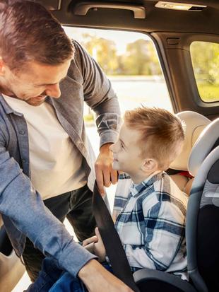 Ein Mann kümmert sich um einen kleinen Jungen in einem Auto und stellt sicher, dass er sicher in einem Kindersitz sitzt.