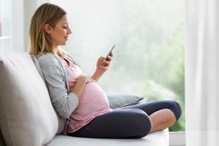 Schwangere Frau sitzt entspannt auf dem Sofa und nutzt auf ihrem Smartphone den HiPP Rechner.
