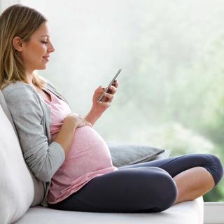 Schwangere Frau sitzt entspannt auf dem Sofa und nutzt auf ihrem Smartphone den HiPP Rechner.