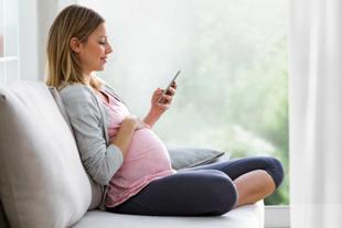 Schwangere Frau sitzt entspannt auf dem Sofa und nutzt auf ihrem Smartphone den HiPP Rechner.