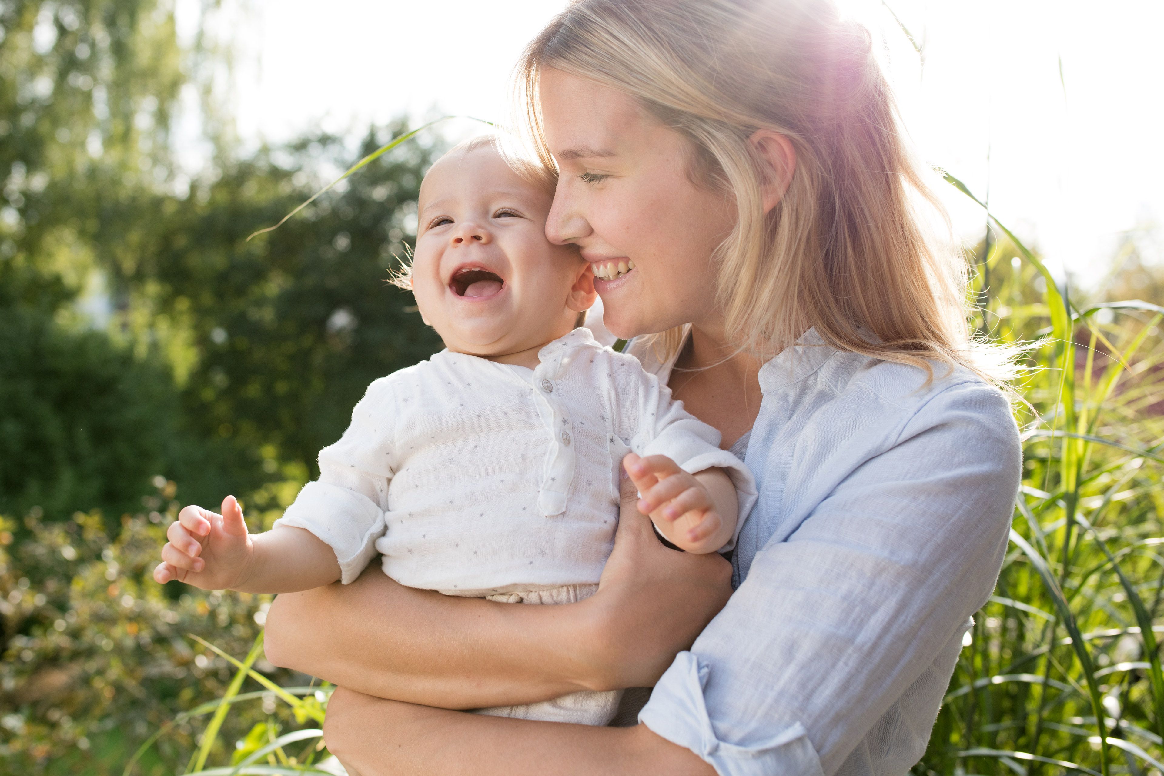 Ein zärtlicher Moment zwischen einer Mutter und ihrem Baby, wobei die Mutter lächelt und das Baby fröhlich lacht.