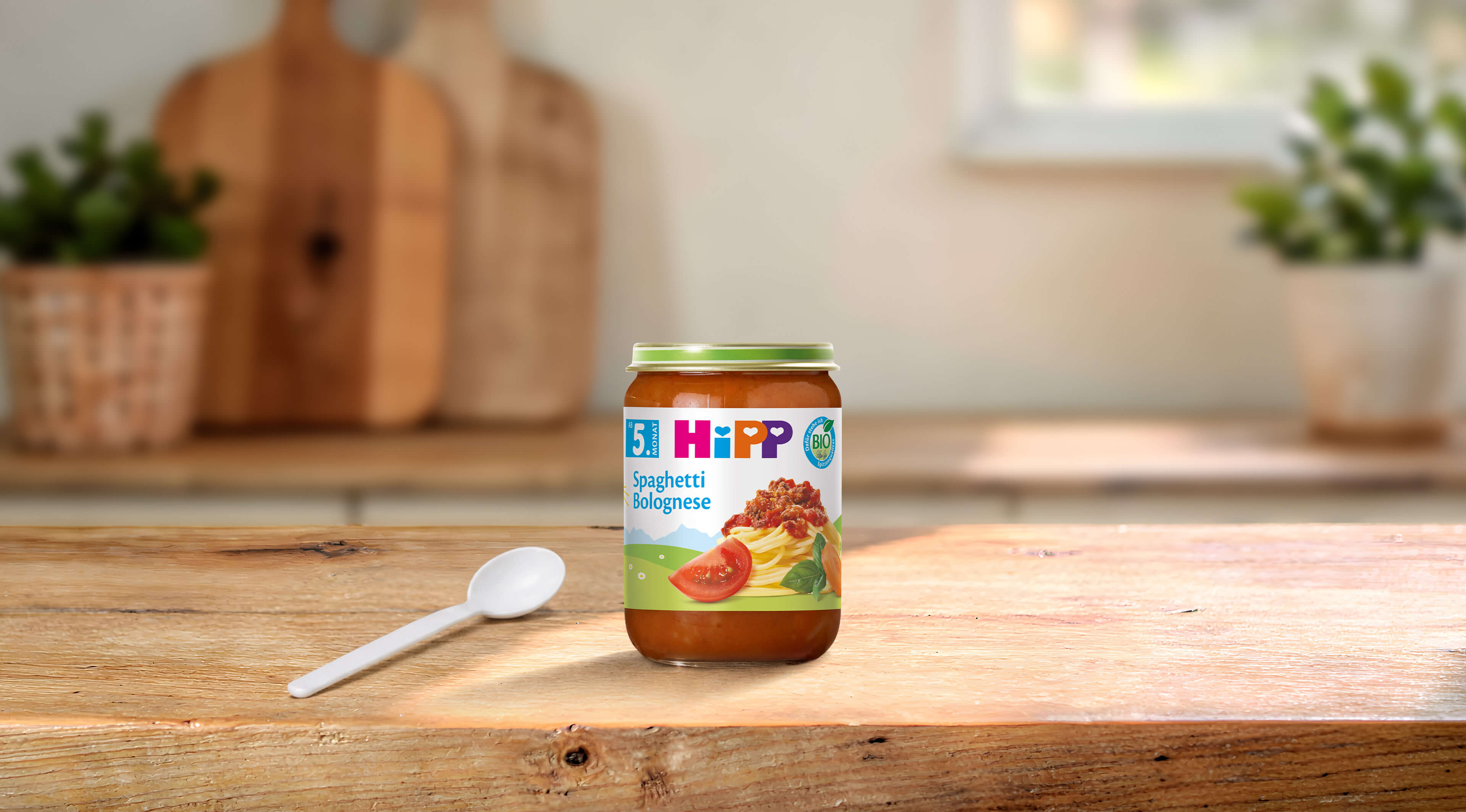 HiPP Bio Babygläschen Spaghetti Bolognese 190g auf Holztisch mit Löffel in heller, gemütlicher Küche