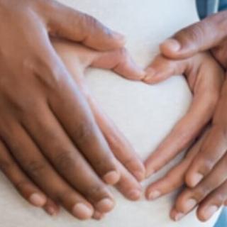 Close-up of hands forming a heart shape on a pregnant belly, symbolizing love and anticipation.