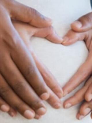 Close-up of hands forming a heart shape on a pregnant belly, symbolizing love and anticipation.
