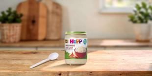 HiPP Bio Milchreis mit Apfel im 190g-Gläschen mit Löffel auf einem Holztisch in einer hellen Küche