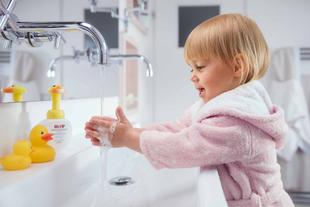 in kleines Kind in einem rosafarbenen Bademantel wäscht sich die Hände unter einem Wasserhahn.