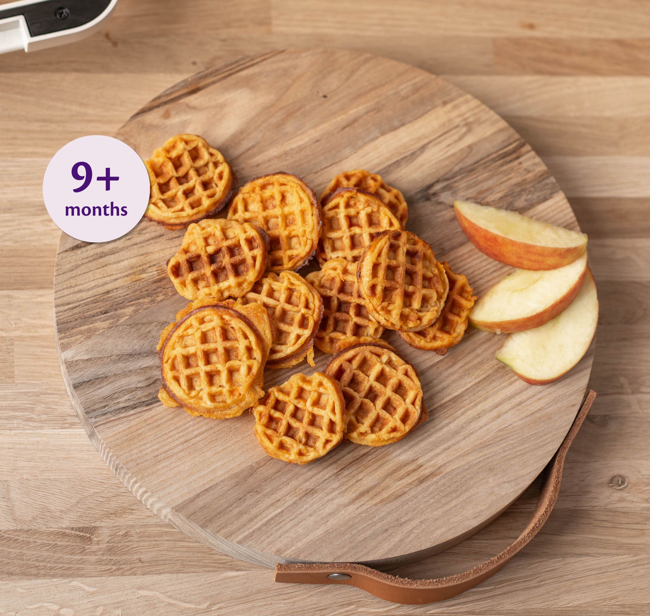 Mini sweet potato and apple waffles on a wooden board with apple slices, labelled suitable for babies 9+ months