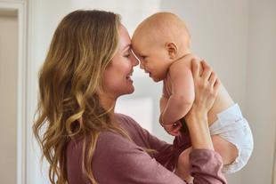 Frau mit langen Haaren hält Baby in Windel nah an ihr Gesicht
