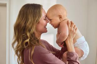 Frau mit langen Haaren hält Baby in Windel nah an ihr Gesicht