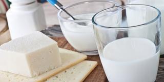 Verschiedene Molkereiprodukte, darunter ein Stück Käse, ein Glas Milch und ein Behälter mit Joghurt, die alle auf einer Holzunterlage platziert sind.