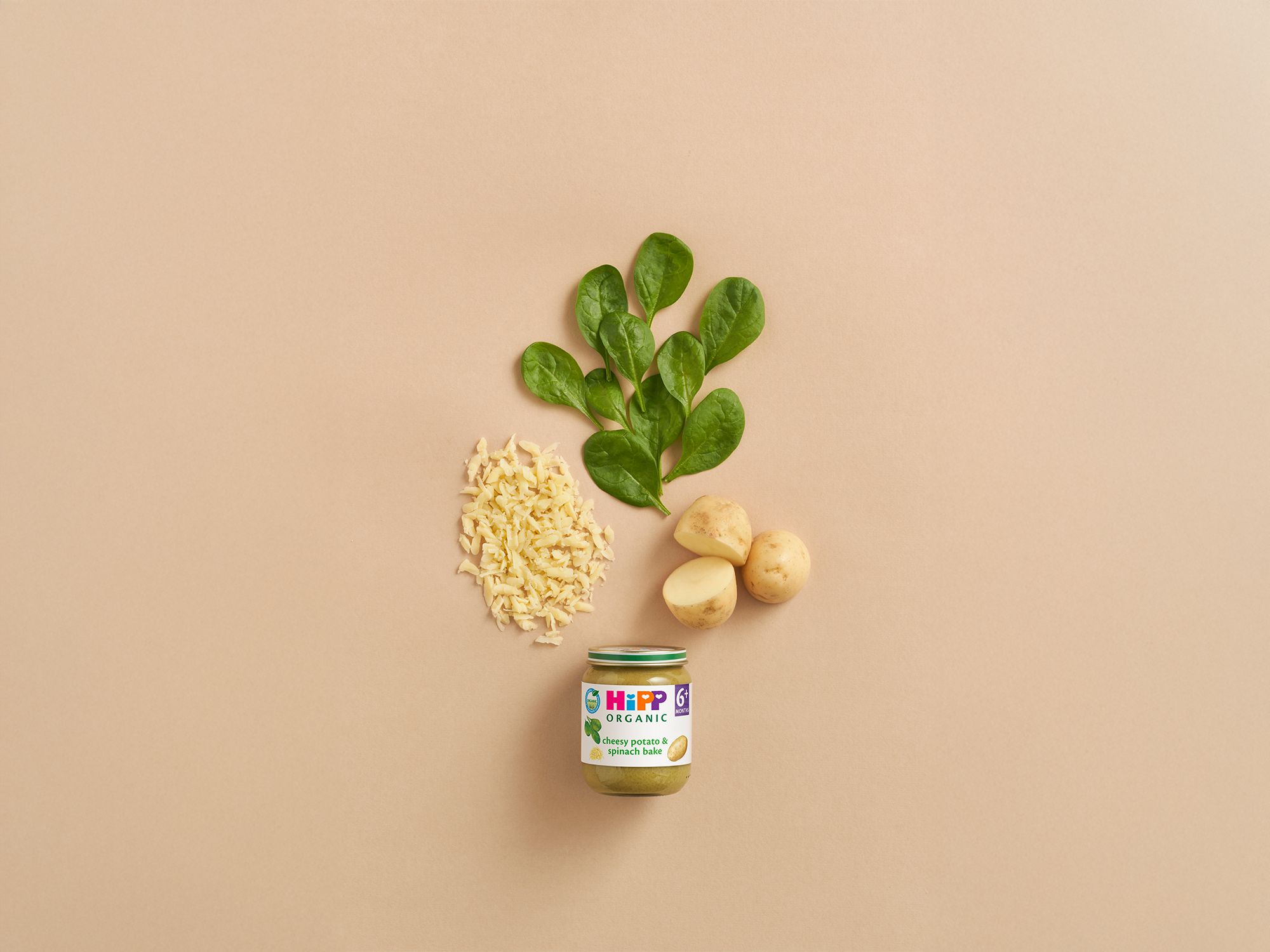 HiPP Organic Cheesy Potato & Spinach Bake jar with spinach leaves, potatoes and grated cheese on a neutral background