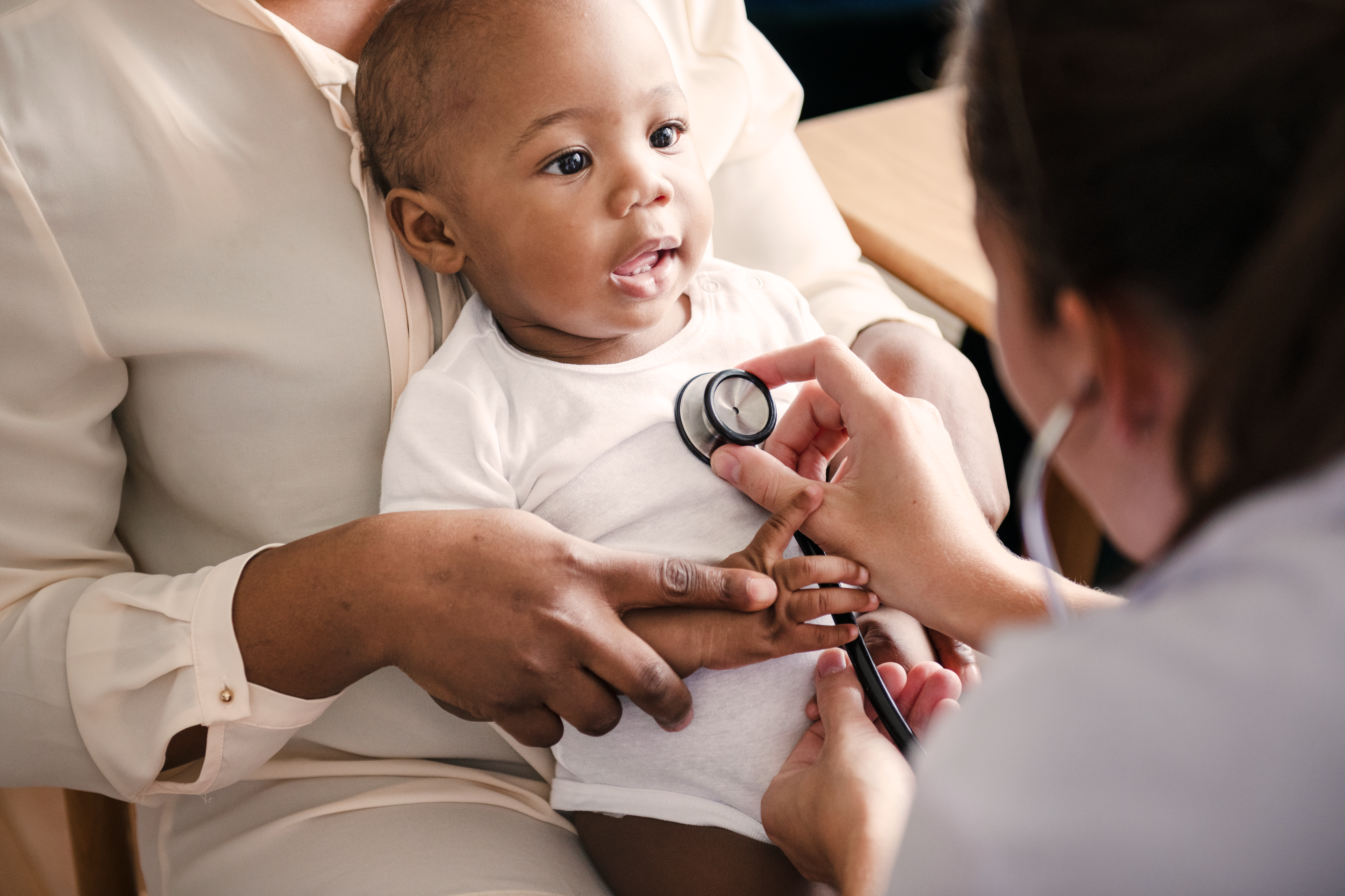 Baby on parent's lap with a Healthcare Professional using a stethoscope
