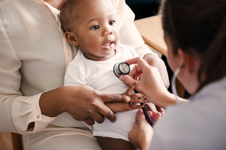 Baby on parent's lap with a Healthcare Professional using a stethoscope