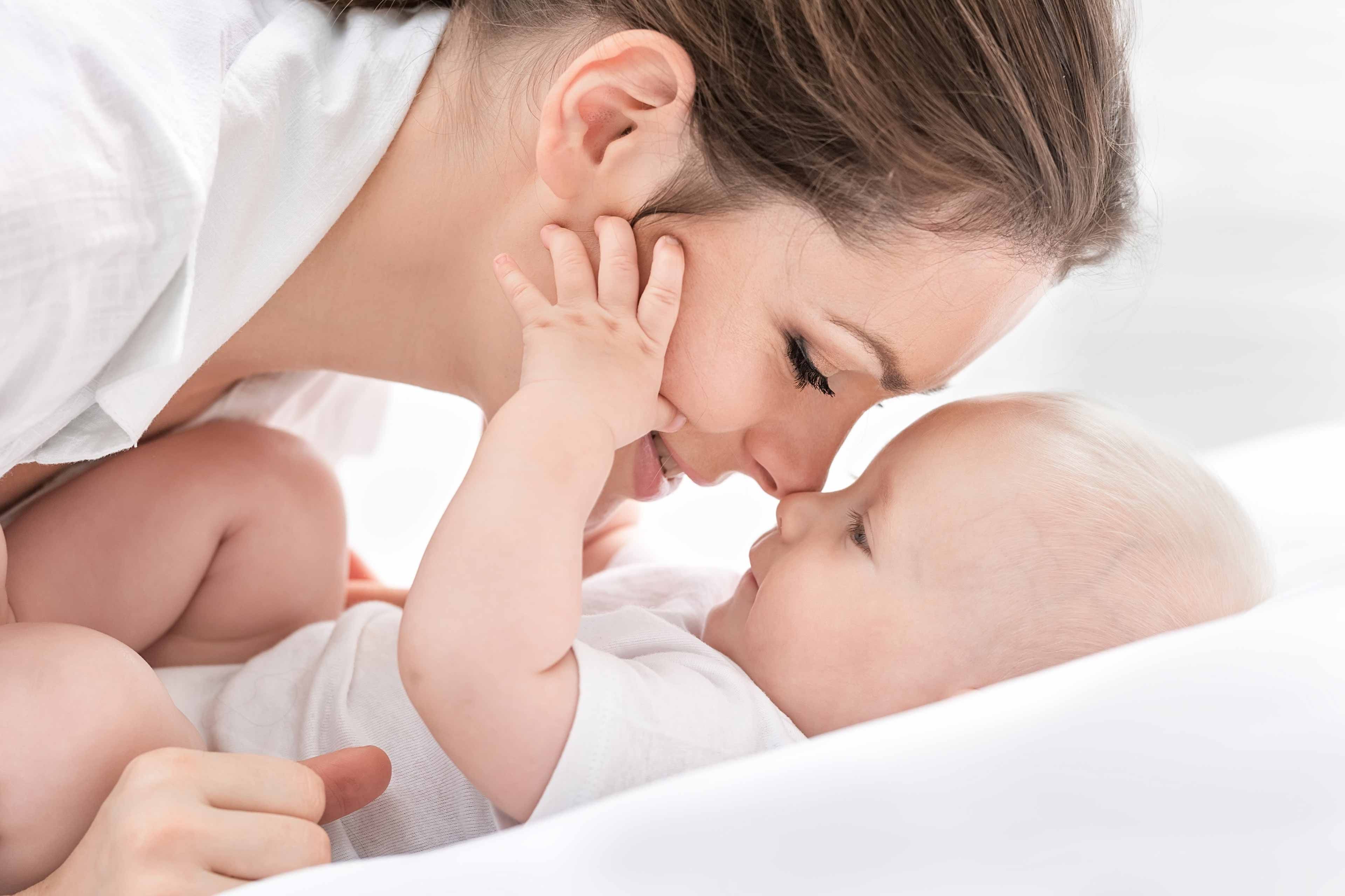 Ein zärtlicher Moment zwischen einer Mutter und ihrem Baby, in dem die Mutter sanft das Gesicht des Babys berührt und damit Gefühle der Liebe und Verbundenheit hervorruft.