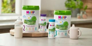 HiPP Organic follow on and growing up milks on a kitchen worktop next to a bottle of milk and a sippy cup
