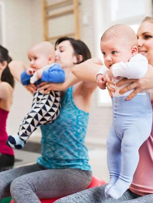 Drei Frauen in einem Fitnessstudio, jede mit einem Baby in der Hand, bei einer Fitnessaktivität.