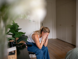 Woman sat on chair in bedroom with head in hands