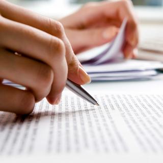 Die Hand einer Person, die einen Stift hält, um auf ein Blatt Papier zu schreiben.