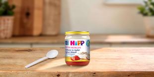 HiPP Guten Morgen Erdbeere in Apfel-Joghurt-Müesli Bio-Gläschen mit Löffel auf einem Holztisch in heller Küche