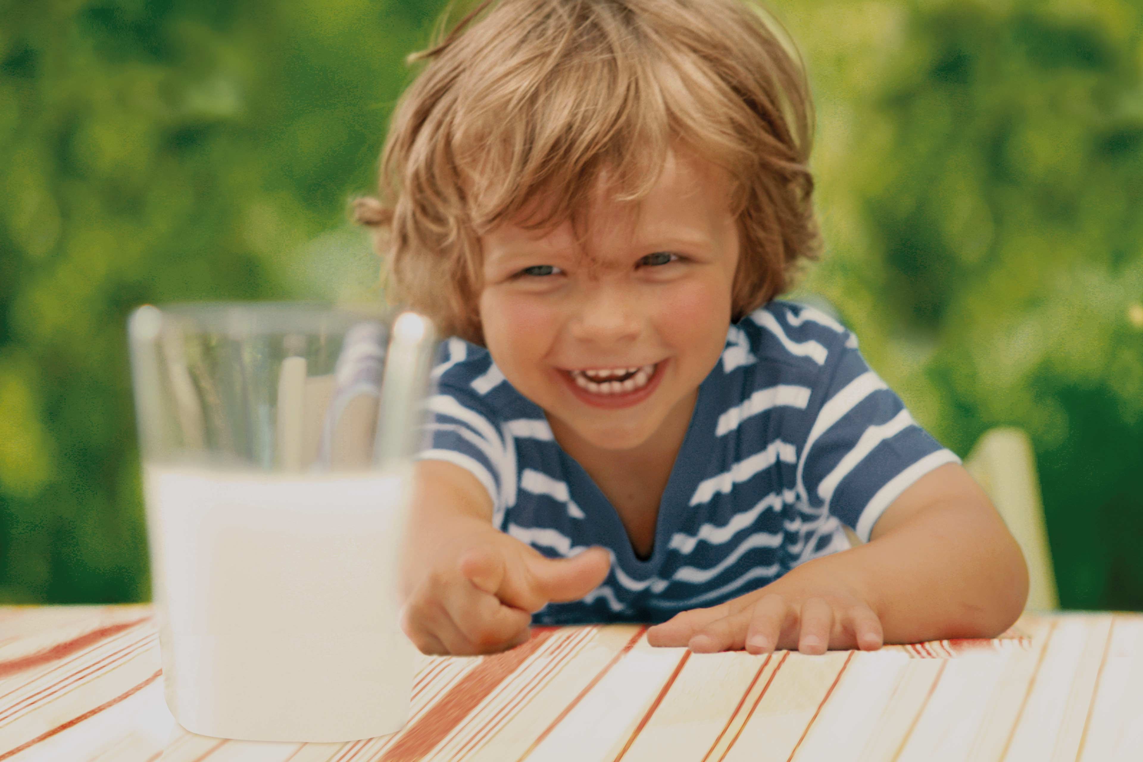 Ein fröhliches Kind, das nach einem Glas Milch greift.