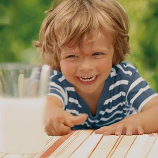 Ein fröhliches Kind, das nach einem Glas Milch greift.