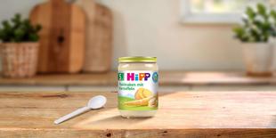 HiPP Bio-Gläschen „Pastinaken mit Kartoffeln“ ab dem 5. Monat mit Löffel auf Holztisch in heller Küche