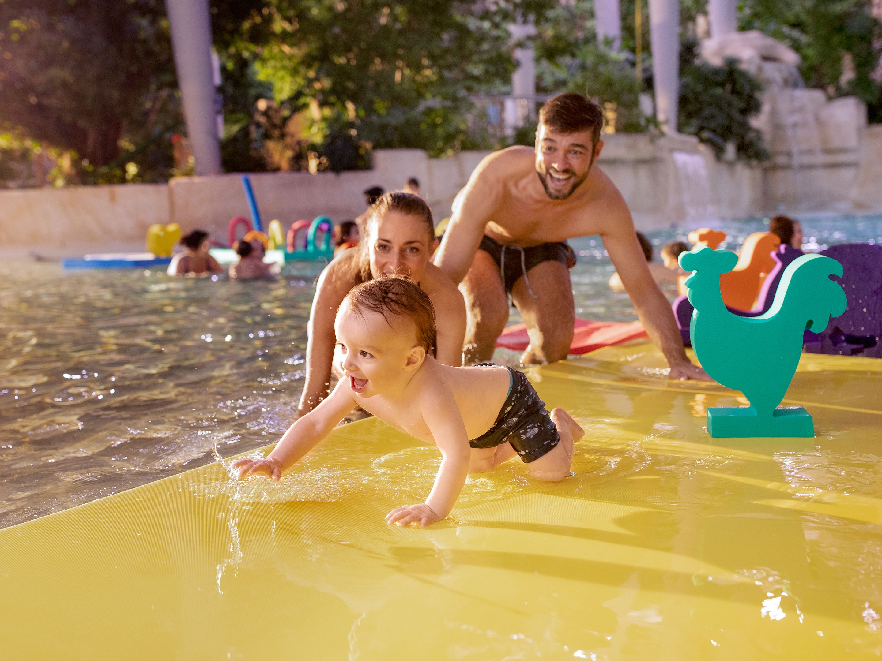 Glückliche Familie mit Kind im tropischen Center-Parcs-Schwimmbad, die gemeinsam im Wasser spielt und lacht