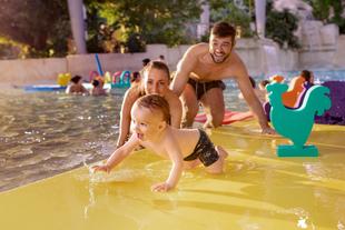 Glückliche Familie mit Kind im tropischen Center-Parcs-Schwimmbad, die gemeinsam im Wasser spielt und lacht