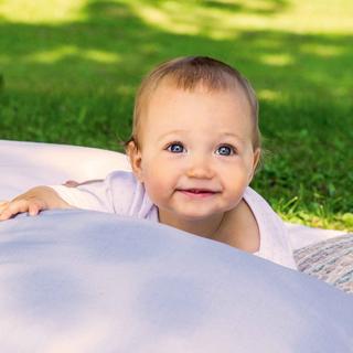 Ein Baby liegt auf einer Decke im Freien, umgeben von Kissen.