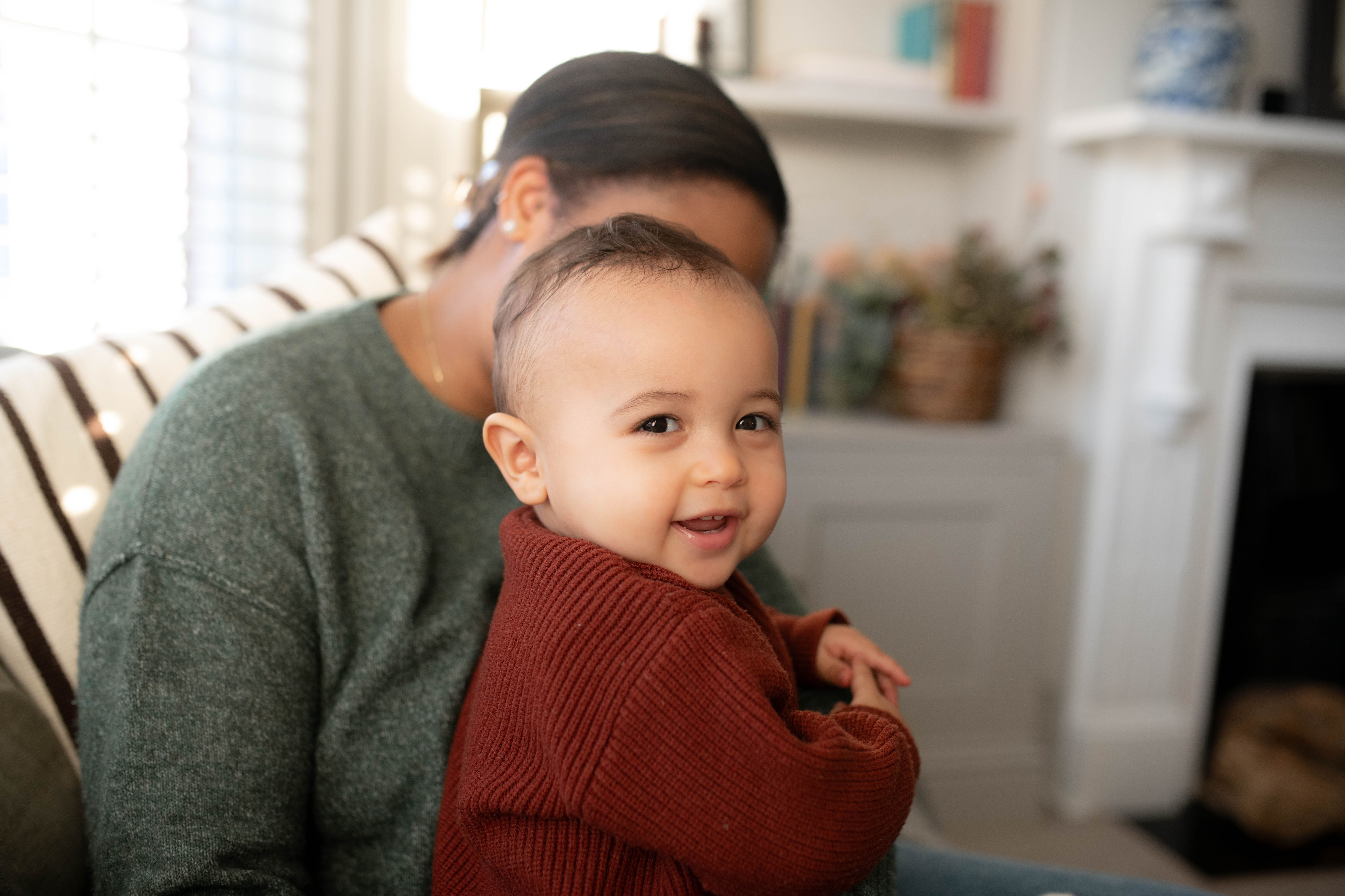 Smiling baby in a cosy jumper sitting on a caregiver’s lap at home
