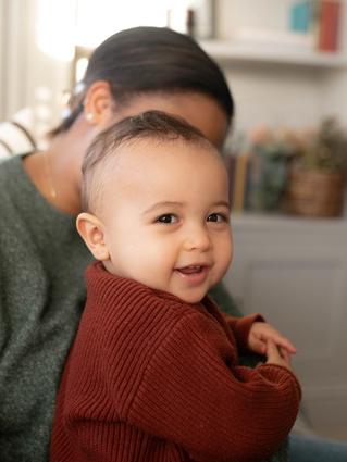 Smiling baby in a cosy jumper sitting on a caregiver’s lap at home