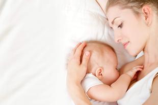 Ein zärtlicher Moment zwischen einer Mutter und ihrem Baby, in dem die Mutter das Baby sanft an sich drückt, während beide auf einer weißen Fläche ruhen.