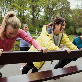 Vier Frauen im Freien, die auf einer Holzbank eine spielerische Tätigkeit ausüben.