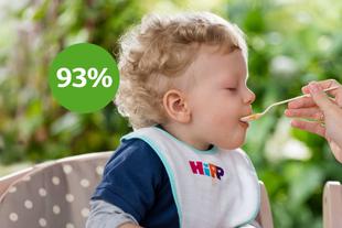 Baby im Hochstuhl mit HiPP-Lätzchen wird mit Löffel gefüttert, daneben grüner Kreis mit „93 %“ Zufriedenheit.