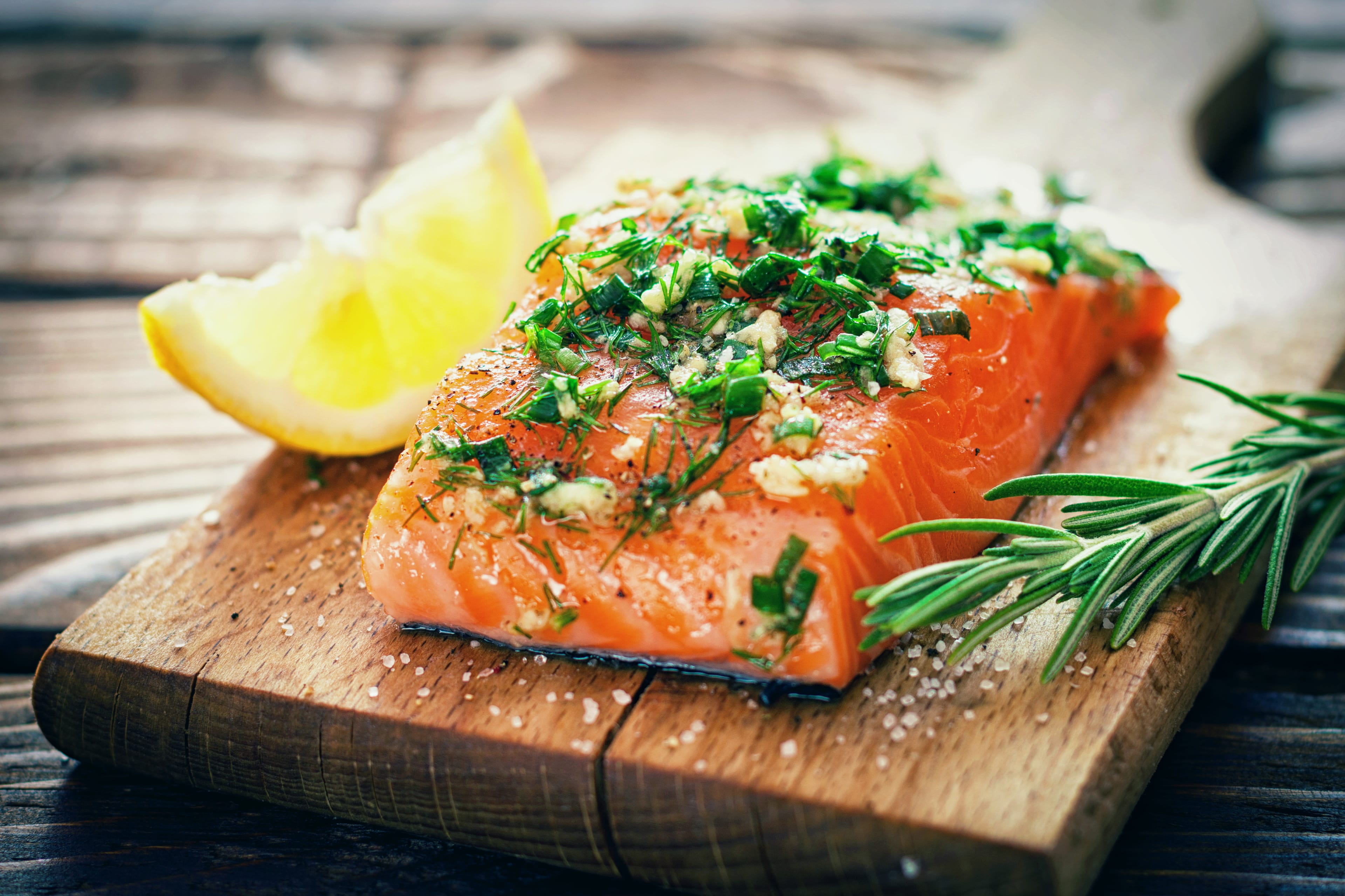 Ein Stück Lachs, mit Kräutern gewürzt und mit Zitrone garniert, auf einem Holzbrett platziert.