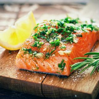 Ein Stück Lachs, mit Kräutern gewürzt und mit Zitrone garniert, auf einem Holzbrett platziert.