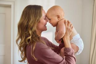 Frau mit langen Haaren hält Baby in Windel nah an ihr Gesicht