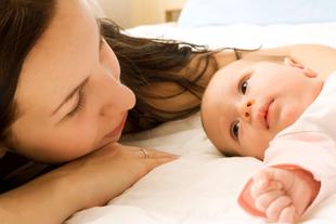 Ein zärtlicher Moment zwischen einer Mutter und ihrem Baby, in dem die Mutter das Baby sanft anschaut, während beide auf einem Bett liegen.